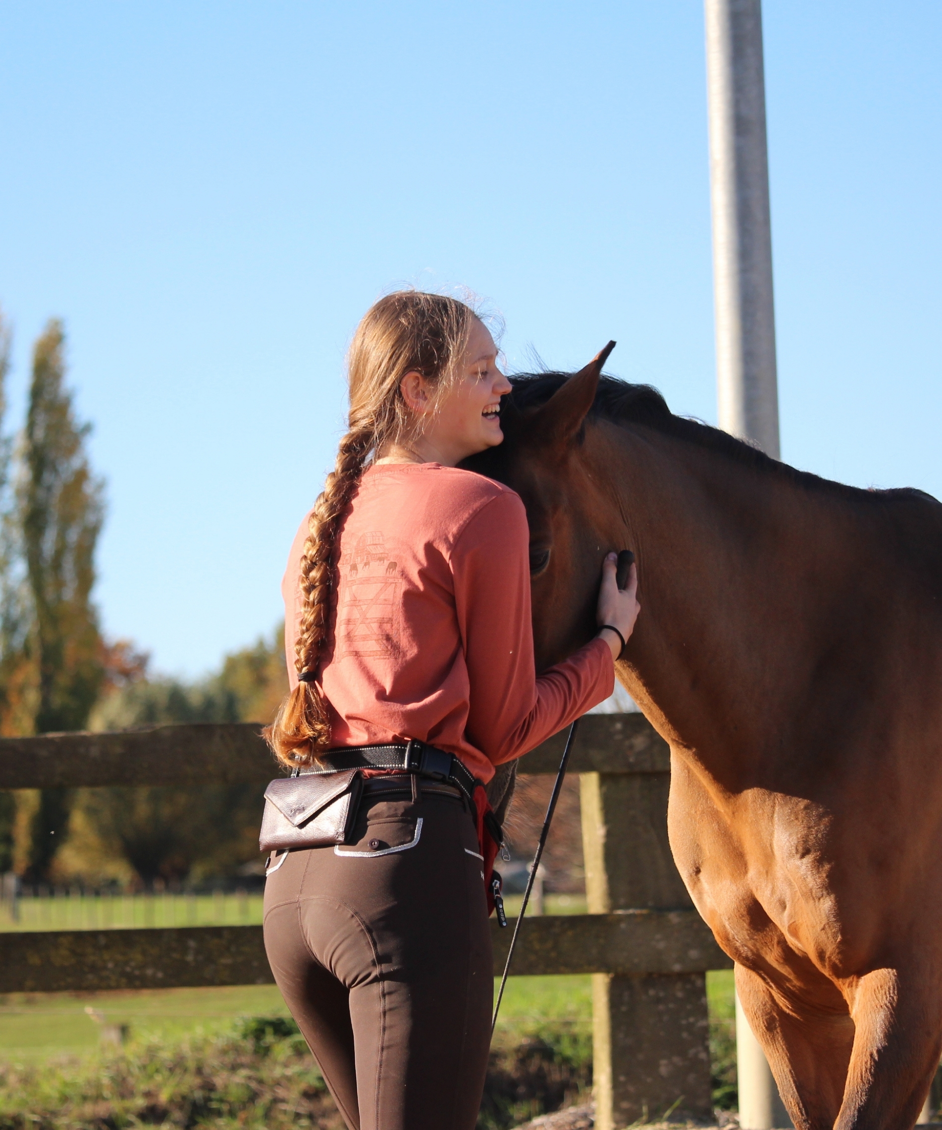 câlin entre un cheval et sa cavalière portant un t-shirt à manches longues couleur rouille pour l'équitation