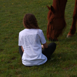 t-shirt d'équitation blanc en coton biologique avec un message engagé contre l'utilisation du pelham porté par une cavalière assise dans le pré des chevaux