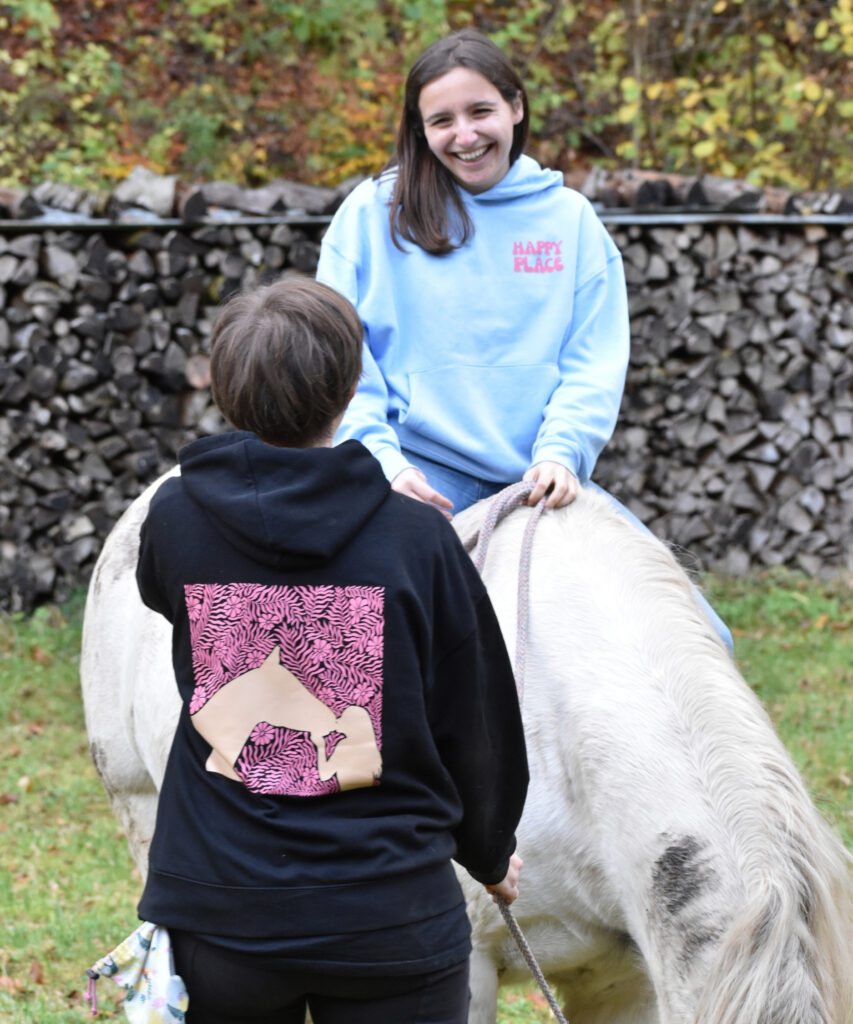 deux cavalières qui portent leurs pulls d'équitation en coton bio noir et bleu ciel avec un message sur l'amour du cheval, une monte à cru sur une jument irish cob