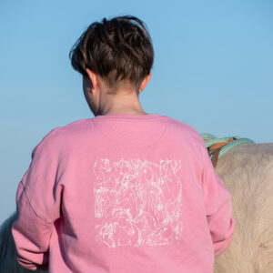 cavalière de dos avec un pull équestre rose en coton biologique illustré de chevaux