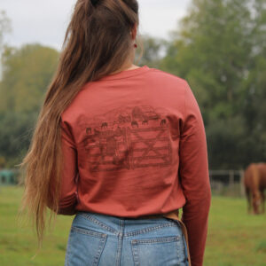 t-shirt à manches longues rouille en coton biologique avec une illustration western porté par une cavalière à l'écurie