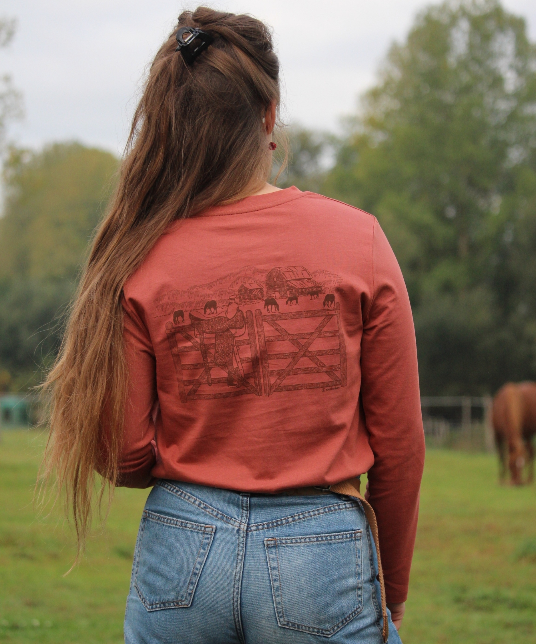 t-shirt à manches longues rouille en coton biologique avec une illustration western porté par une cavalière à l'écurie
