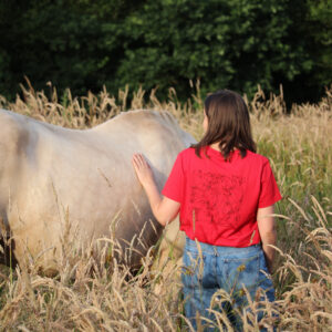 cavalière avec son t-shirt en coton biologique rouge avec une illustration douce et engagée et son cheval palomino dans un champ de blé doré