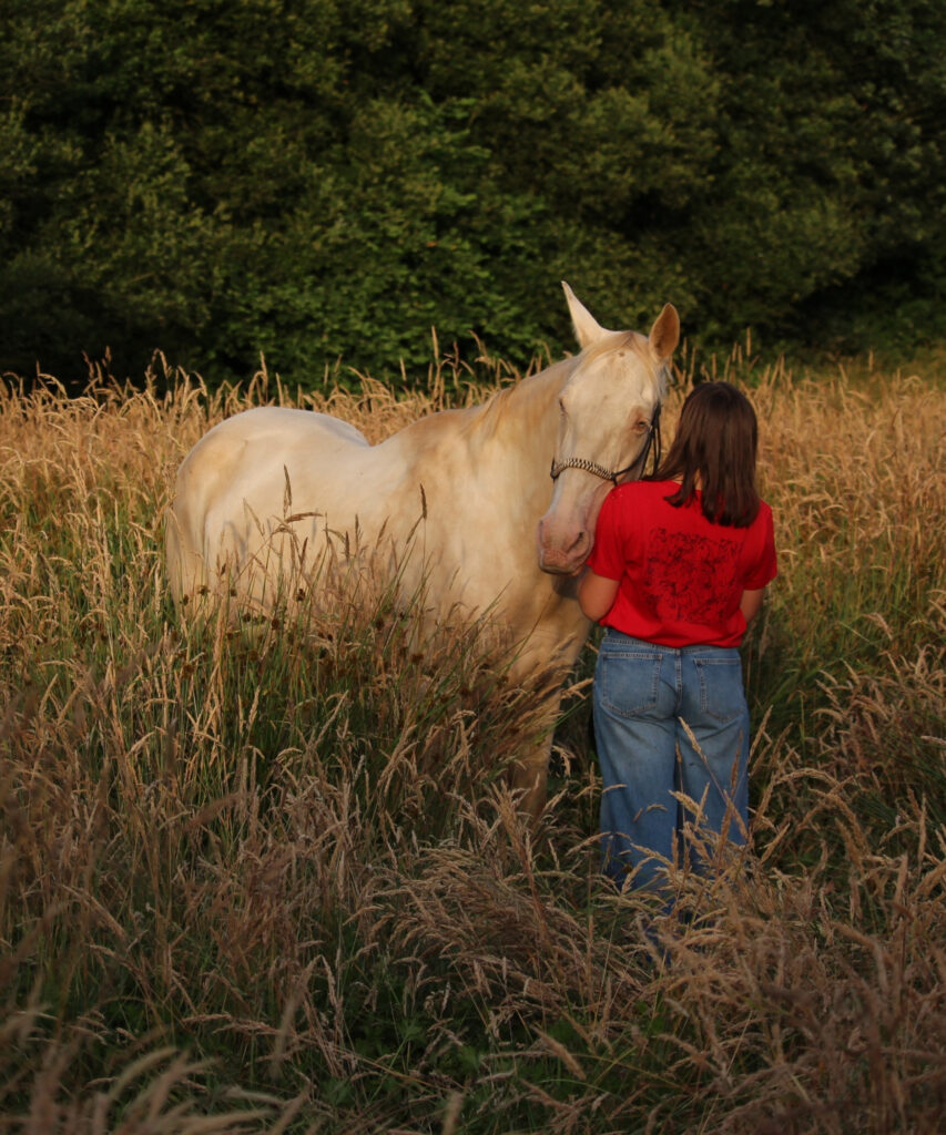 cavalière avec son t-shirt en coton biologique rouge avec une illustration douce et engagée et son cheval palomino dans un champ de blé doré